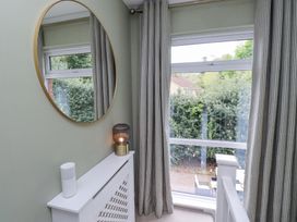 A corner with a round mirror above a white radiator cover and a window with striped curtains at Sparrow House in Alnwick