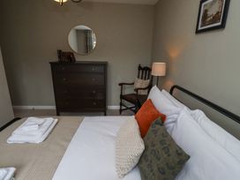 A bedroom with a bed featuring multiple pillows and folded towels a wooden dresser with books and a round mirror above a wooden chair with a cushion a bedside lamp and a framed picture on the wall at Sparrow House in Alnwick