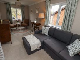 A living room with a gray sofa, two armchairs, a wooden table with flowers, a floor lamp, and patterned curtains at Sparrow House in Alnwick