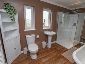 A bathroom with a white toilet, pedestal sink, glass shower enclosure, white cabinet with plant, and wood floor at Sparrow House in Alnwick