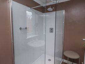A bathroom with a glass shower enclosure a round side table and brown walls at Sparrow House in Alnwick