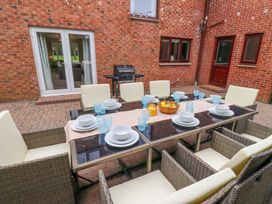 An outdoor dining area with a glass table set with plates bowls and blue glasses surrounded by wicker chairs with cushions at Sparrow House in Alnwick