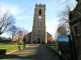The exterior of a stone church with a clock tower and surrounding trees and driveway at Sparrow House in Alnwick