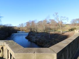 A river flowing past leafless trees with a stone bridge railing in the foreground at Sparrow House in Alnwick