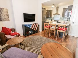 A living room with a brown armchair and red cushions a wooden coffee table a small kitchen with three wooden bar stools at the counter and a television mounted on the wall at DownTown - Manhattan House in Llandudno