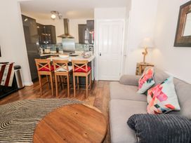 An open plan living room and kitchen with a gray sofa with colorful pillows wooden chairs around a kitchen island and a round wooden coffee table at DownTown - Manhattan House in Llandudno