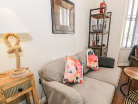 A living room with a grey sofa with patterned cushions a wooden side table with a rope lamp a shelving unit and a window at DownTown - Manhattan House in Llandudno