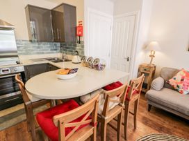 A kitchen with a white countertop island and wooden stools with cushions next to a gray sofa with a patterned cushion at DownTown - Manhattan House in Llandudno