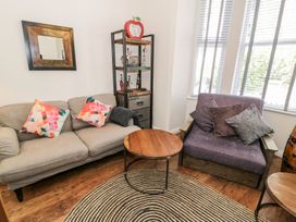 A living room with a beige sofa and a purple armchair with pillows around a round wooden coffee table at DownTown - Manhattan House in Llandudno