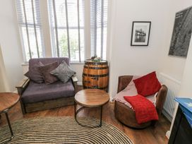 A sitting area with two armchairs a round wooden coffee table a barrel side table and wall art at DownTown - Manhattan House in Llandudno