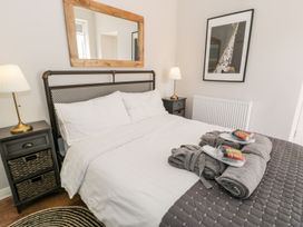 A bedroom with a bed white bedding bedside tables with lamps a mirror above the headboard and a framed picture on the wall at DownTown - Manhattan House in Llandudno