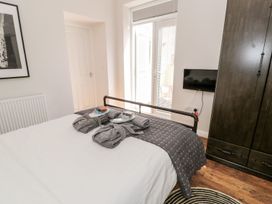 A bedroom with a bed, folded towels, robes, a mounted television, a wooden wardrobe, a door leading outside, and a framed picture on the wall at DownTown - Manhattan House in Llandudno
