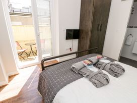 A bedroom with a bed and two robes, a wardrobe, a wall-mounted TV, and a door leading to a small balcony with chairs and a table at DownTown - Manhattan House in Llandudno