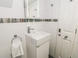 A small bathroom with a white sink cabinet a mirror towel hanging on a ring and a white door at DownTown - Manhattan House in Llandudno