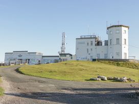 A white multi-section building on a hill with antennas a gravel road and green grass at DownTown - Manhattan House in Llandudno