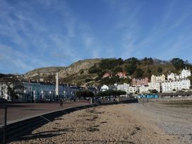 A sandy beach with a paved promenade and buildings at the foot of a rocky hill at DownTown - Manhattan House in Llandudno