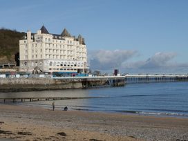 A beach with two people near the shore and a large hotel building next to a pier at DownTown - Manhattan House in Llandudno