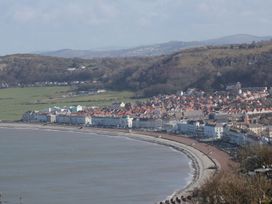 A curved coastline with a promenade and buildings along the shore with hills in the background at DownTown - Manhattan House Llandudno
