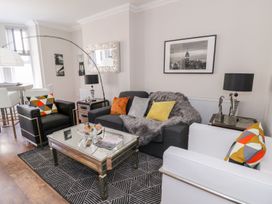 A living room with black and white armchairs a dark sofa with colorful cushions a glass coffee table and framed pictures on the walls at MidTown - Manhattan House in Llandudno