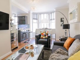 A living room with a black armchair a gray sofa a glass coffee table and a kitchen area with bar stools at MidTown - Manhattan House in Llandudno