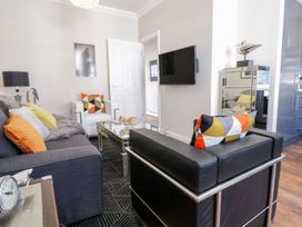 A living room with a wall-mounted television a glass coffee table and a black leather chair at MidTown - Manhattan House in Llandudno