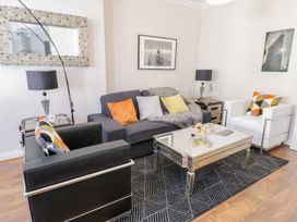 A living room with black and white armchairs a grey sofa with cushions a glass coffee table and framed pictures on the wall at MidTown - Manhattan House in Llandudno