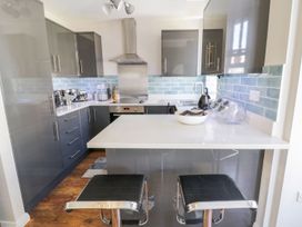 A kitchen with grey cabinets a white countertop blue tiled backsplash and two black stools at MidTown - Manhattan House in Llandudno