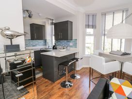 A kitchen and dining area with black cabinets a blue tiled backsplash and white chairs at MidTown - Manhattan House in Llandudno