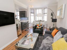 A living room with a sofa a black armchair a glass coffee table and a dining area with windows at MidTown - Manhattan House in Llandudno