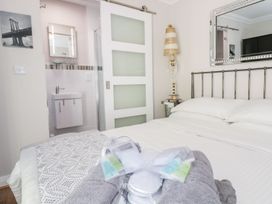 A bedroom with a bed and white bedding a bedside table with a lamp and a sliding door leading to a bathroom at MidTown - Manhattan House in Llandudno
