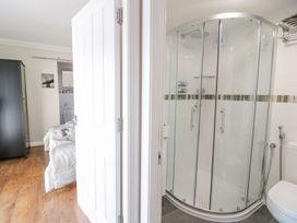 A corner shower with glass doors in a bathroom next to a partially open door revealing a bedroom with a bed and wardrobe at MidTown - Manhattan House in Llandudno