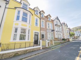 A row of attached multi-story houses with bay windows along a sloped street at UpTown - Manhattan House in Llandudno