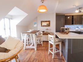 A dining area with a wooden table and chairs next to a kitchen island with bar stools at UpTown - Manhattan House in Llandudno