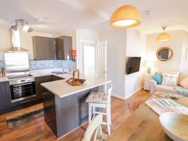 A kitchen with grey cabinets and a breakfast bar next to a sitting area with a beige sofa and a wall-mounted TV at UpTown - Manhattan House in Llandudno