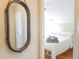 A bedroom with a white bed frame and bed linens with towels stacked on the bed seen through a doorway with a wall mirror on the left at UpTown - Manhattan House in Llandudno