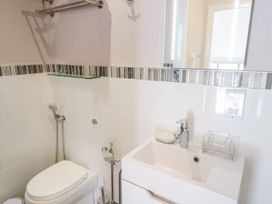 A bathroom with a white toilet a white sink with a faucet a soap dish a glass shelf and tiles with a vertical stripe pattern at UpTown - Manhattan House in Llandudno