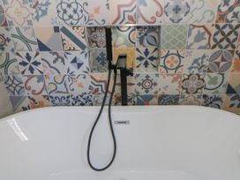A bathtub with a faucet and patterned wall tiles at Island House Aberaeron
