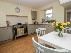 A kitchen with grey cabinets a stove a white table yellow roses on the table and a window with plants at 7 New Street in Sedbergh