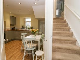 A kitchen with wooden floor a white dining table and chairs yellow flowers on the table and a carpeted staircase at 7 New Street in Sedbergh