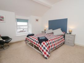A bedroom with a bed with a checkered duvet two bedside tables with lamps a window and a black chair at 7 New Street in Sedbergh