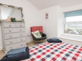 A bedroom with a bed covered in red white and blue checkered bedding and folded towels on it a grey chest of drawers with a mirror and flowers a black chair with a butterfly cushion and red throw and a window with a blue blind at 7 New Street in Sedbergh