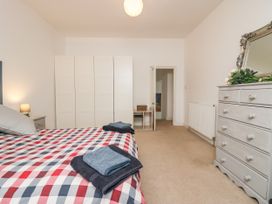 A bedroom with a bed with checkered bedding a chest of drawers with a mirror and flowers a wardrobe and a door at 7 New Street in Sedbergh