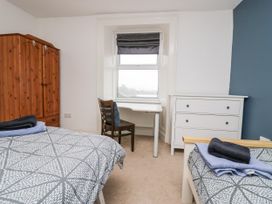 A bedroom with two beds a wooden wardrobe a desk and chair under a window and a white chest of drawers at 7 New Street in Sedbergh