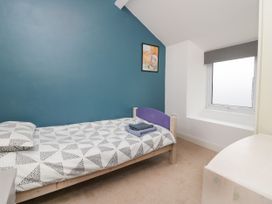 A bedroom with a single bed against a blue wall a window with a grey blind and a wooden dresser at 7 New Street in Sedbergh