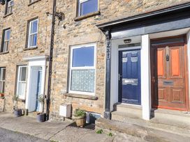 A stone exterior of a building with blue and brown front doors and potted plants on the pavement at 7 New Street in Sedbergh