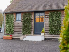 The exterior of a wooden cottage with a blue door steps and trellises with green plants at Bee Cottage in Ottinge near Lyminge