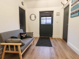 An entryway with a wooden framed gray sofa with cushions a black door a black mat on wood flooring and two black doors on the sides at Bee Cottage in Ottinge near Lyminge