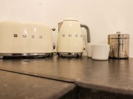 A kitchen countertop with a cream SMEG toaster, SMEG kettle, two white cups, and a stainless steel coffee container at Bee Cottage in Ottinge near Lyminge