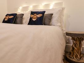 A bedroom with a white bed and pillows with bee designs next to a wooden side table at Bee Cottage in Ottinge near Lyminge