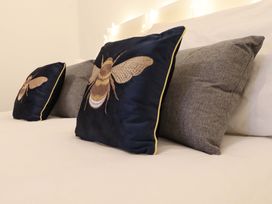 Two decorative pillows with bee embroidery and two plain grey pillows on a bed at Bee Cottage in Ottinge near Lyminge